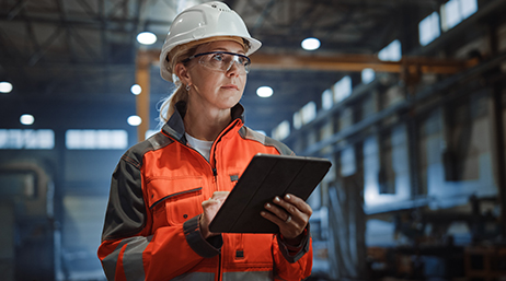 A person wearing a safety vest and hard hat using a tablet in a warehouse