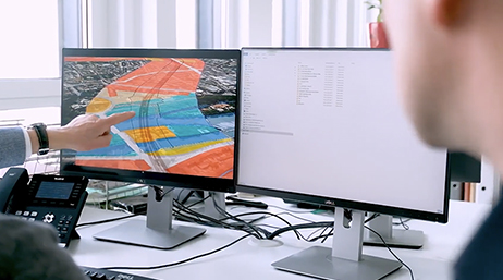 People sitting around and pointing to a dual computer monitor in an office