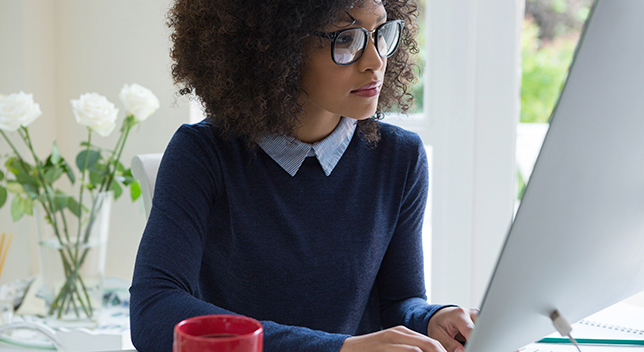 Jeune femme avec des lunettes regardant un grand écran d’ordinateur argenté sur un bureau