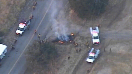 Vista aérea de um incêndio na beira de uma rodovia e vários veículos de resposta a emergências