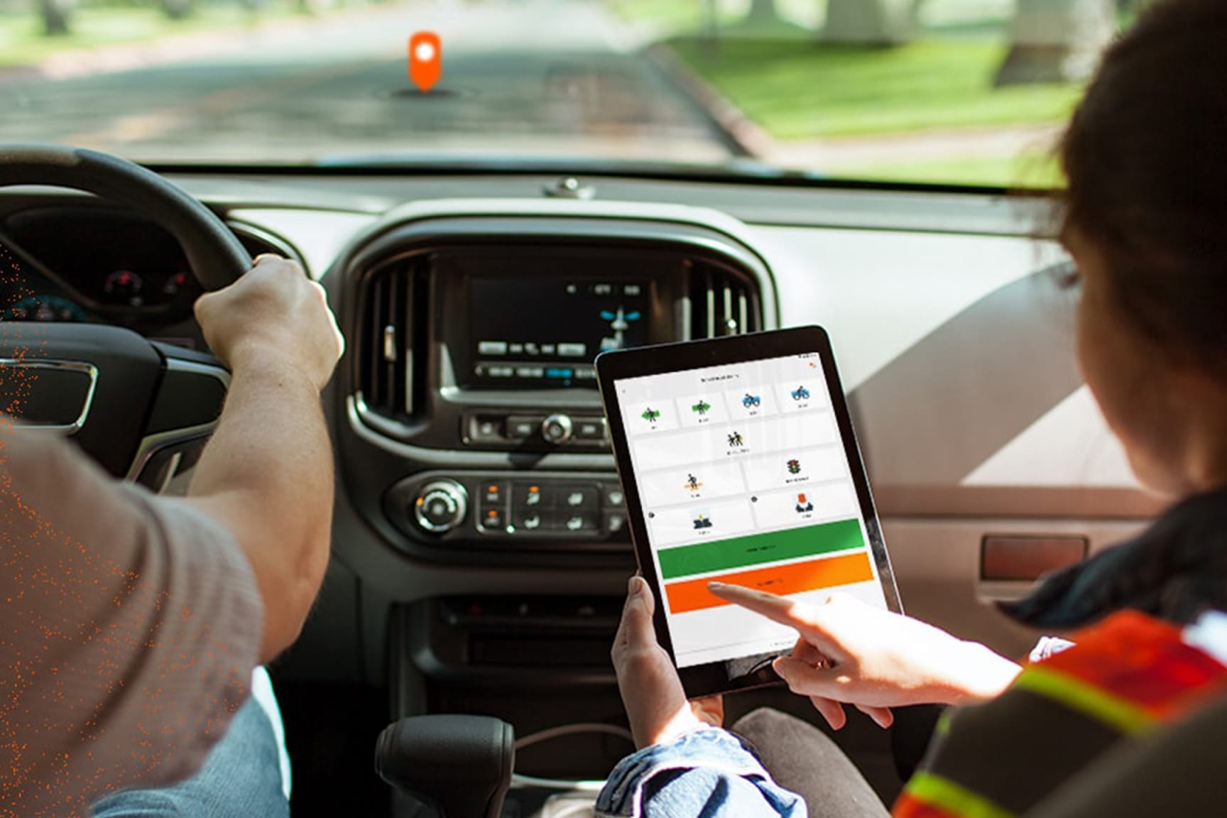 View from rear middle seat - Two people in a car, one driving the other holding a tablet displaying large data capture buttons