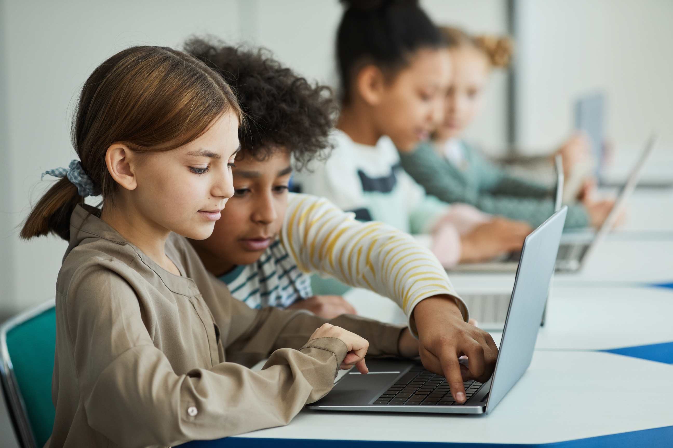 Young students on a laptop sitting at a table in a classroom. 