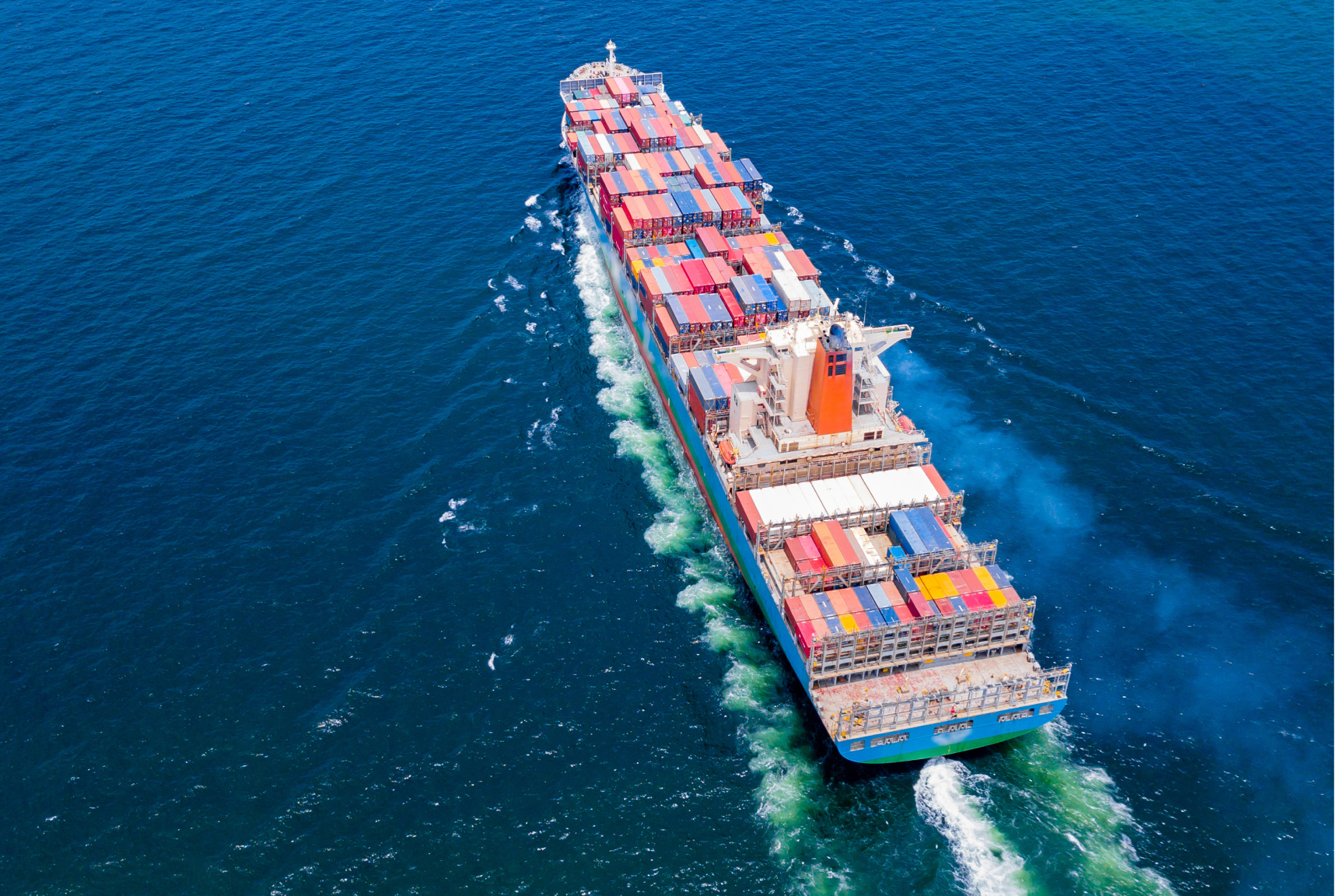 The iamge shows a container ship from a bird's eye view. The ship is carrying a large number of containers, and the water is a deep blue color.