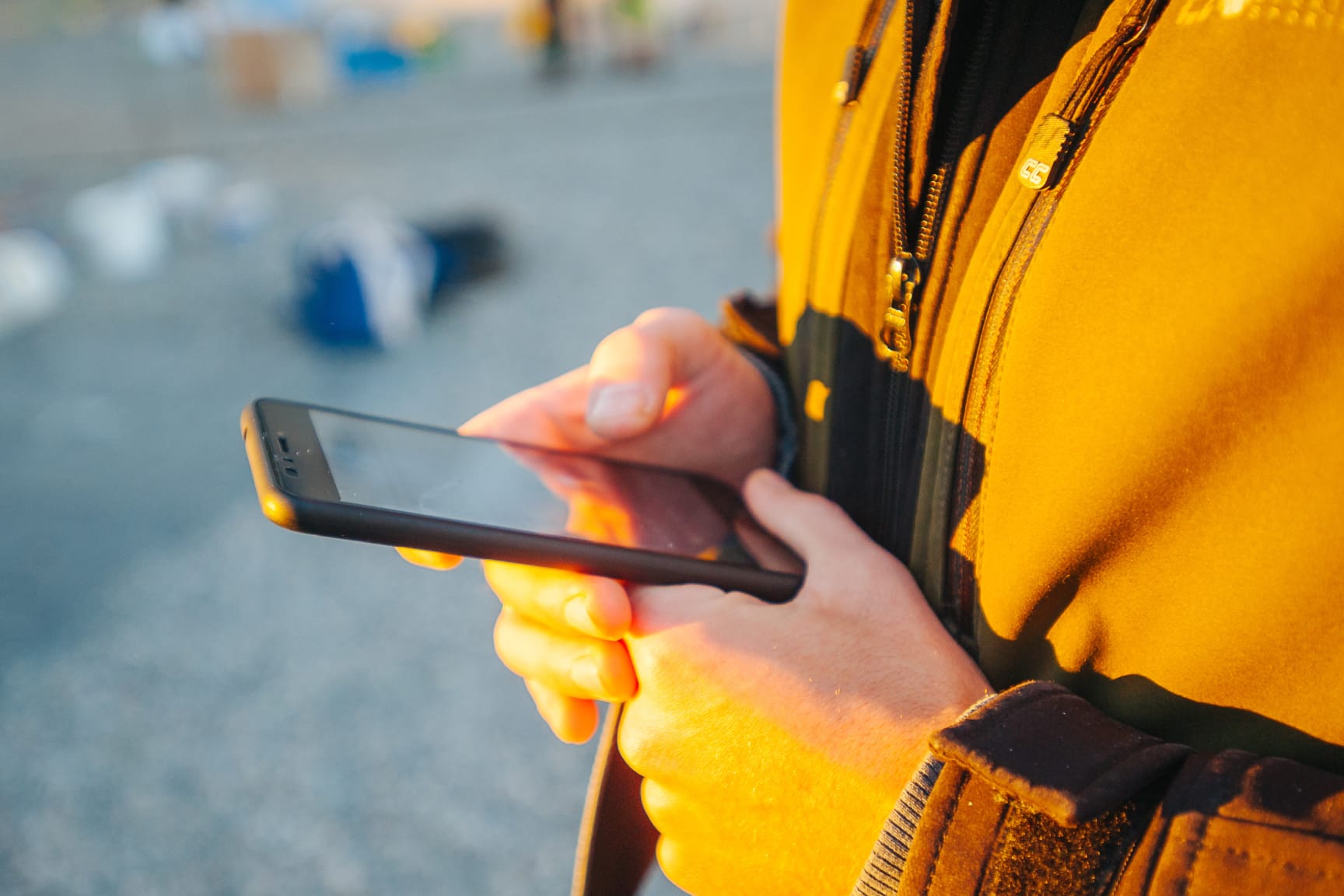 Blurred image of worker standing outdoors holding and reading the screen of a mobile phone.