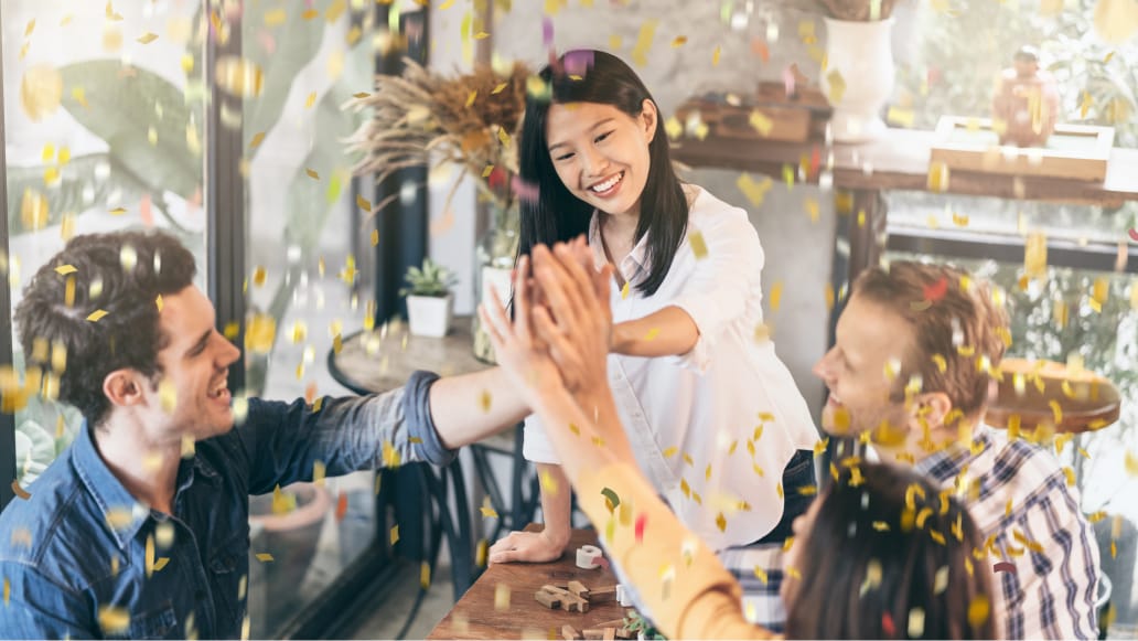 Blurred image of people celebrating, confetti in the air, two people are doing a high five hand in the air.