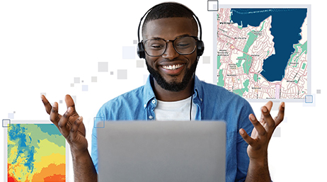 A person using a laptop and headset and smiling with two different maps in the background