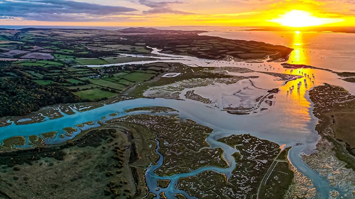 A coastal network of water ways spread across a lush landscape with a brilliant sun rising on the horizon