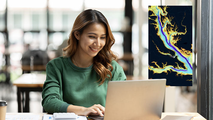 A woman smiling while looking at a laptop which is displaying a colorful map