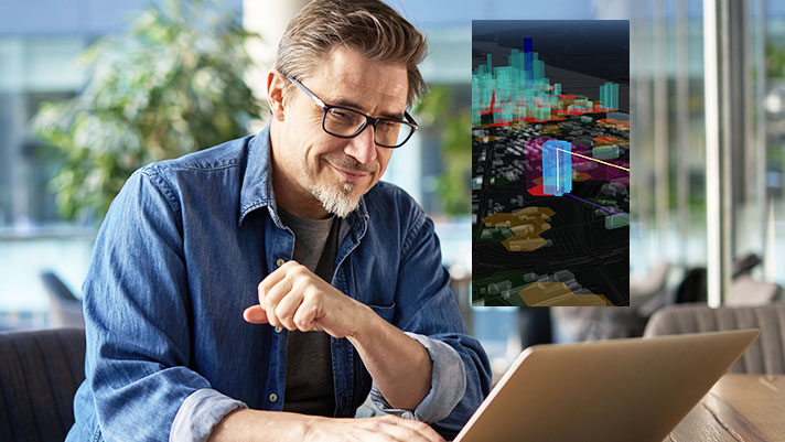 A man wearing glasses looking at a laptop which is displaying a detailed virtual city