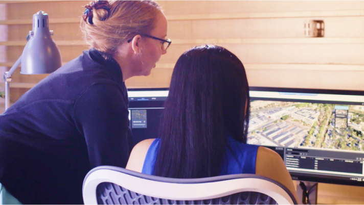 Two women at a desk looking at a computer monitor and collaborating on a 3D map