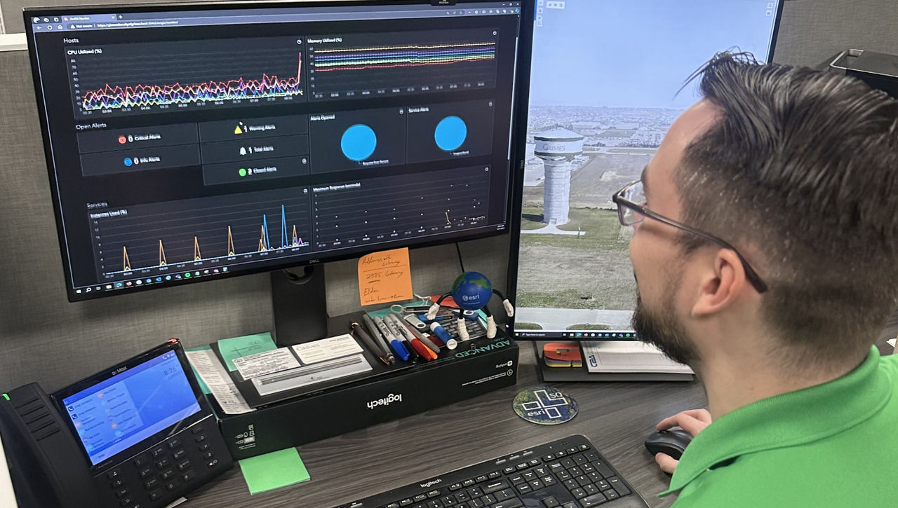 Greg Jameson, a GIS technician for the City of Grimes, is examining ArcGIS Monitor in the morning to detect any alerts from overnight. The visual representation includes a spike in CPU utilization (upper left) and changes in service instances (lower left) as staff arrive.