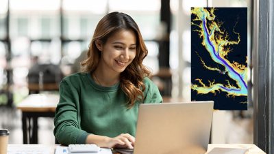 A woman smiling while looking at a laptop which is displaying a colorful map