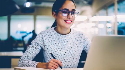 Uma pessoa sorrindo e usando um laptop e uma caneta em um escritório moderno