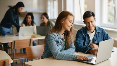 Dois estudantes sentados em uma mesa usando um laptop juntos e sorrindo