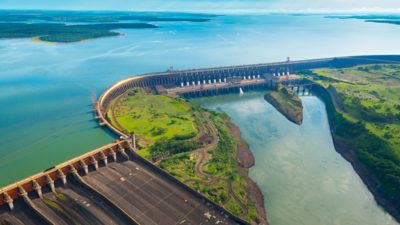 Uma enorme barragem hidrelétrica com torres elétricas e linhas de energia saindo da barragem sobre um corpo d'água